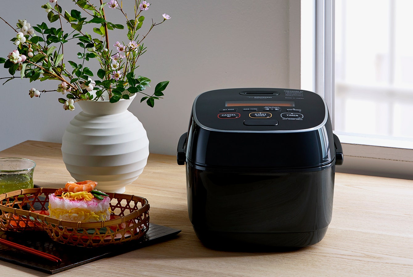 Zojirushi Rice Cooker on a kitchen table next to a plant and food items